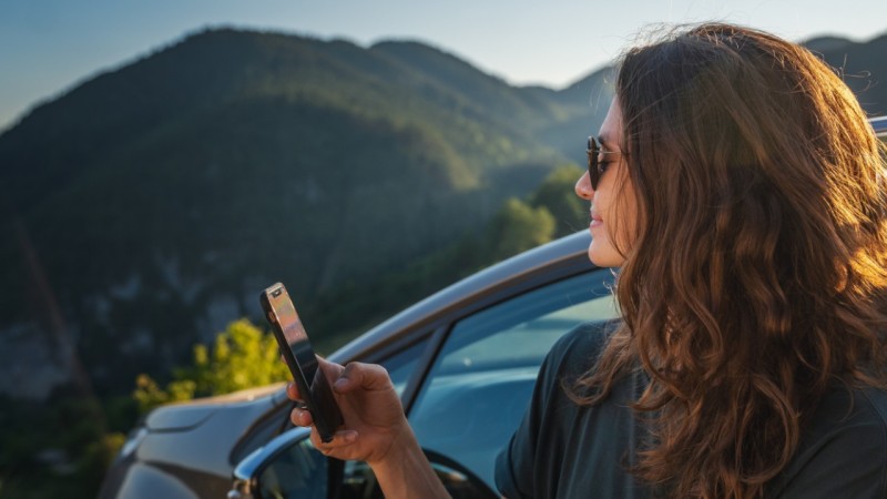 woman holding mobile next to a car